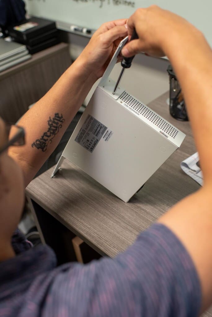 Close up photo of an Ascend associate fixing a Fortinet box with a screwdriver