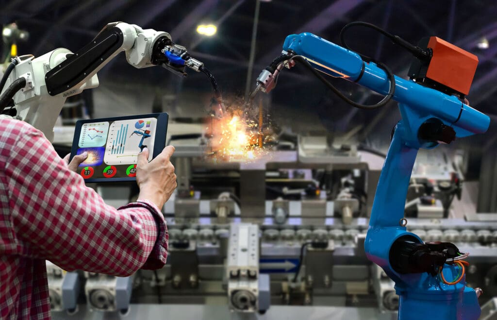 Worker holding tablet monitoring welding robot on an assembly line
